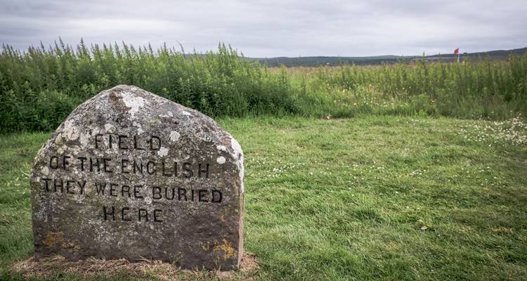 Marqueur de tombe en pierre gravée dans un large champ herbeux sous des nuages gris sur le champ de bataille historique de Culloden.