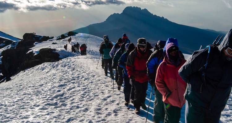 Un groupe d'alpinistes faisant de la randonnée sur un sentier de montagne enneigé avec une vue pittoresque d'un sommet montagneux en arrière-plan.