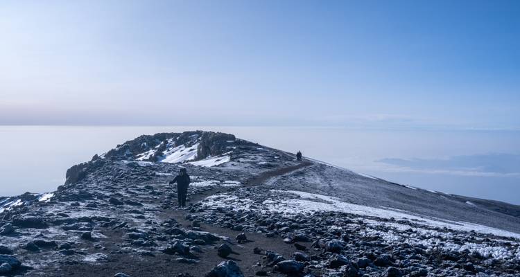 Un paysage montagneux rocheux et enneigé avec des nuages distants et un ciel dégagé.