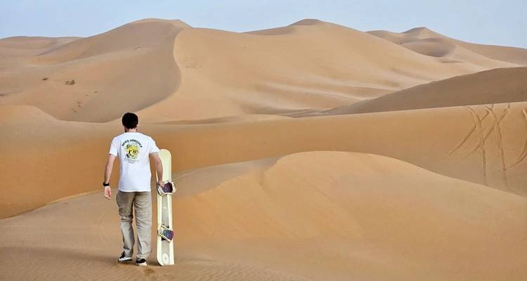 Person with a sandboard walking in the desert.