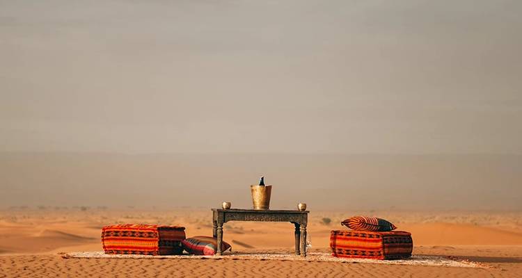 Desert setup with cushions and a table amid sand dunes.