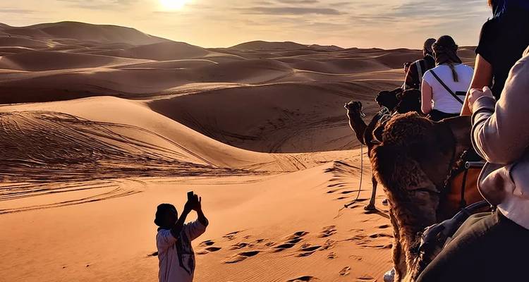 People riding camels at sunset in the desert.
