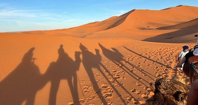 Shadow of camel riders on sand dunes.