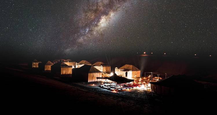 Glowing tents under a starry night sky in the desert.