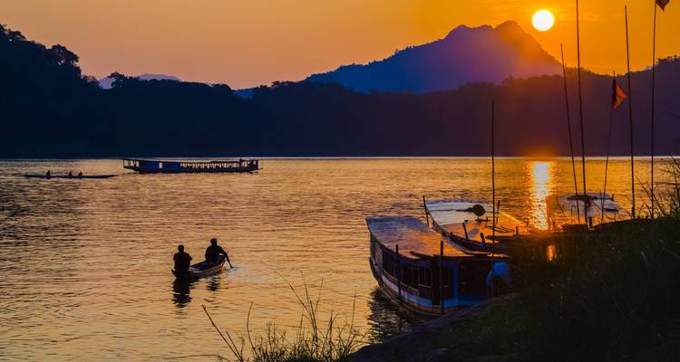 Gesilhouetteerde mensen op een rivier bij zonsondergang.