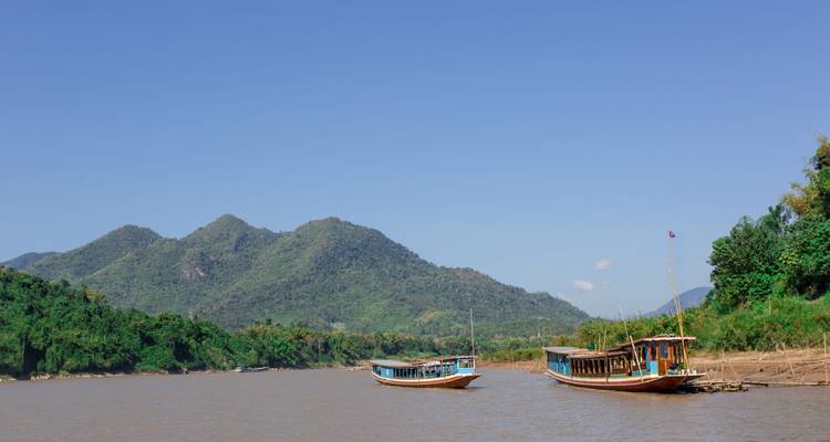 Two boats on a river against a backdrop of mountains.