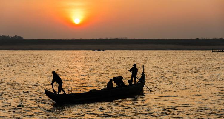 Silhouetted boat on a river at sunset with an orange sky.