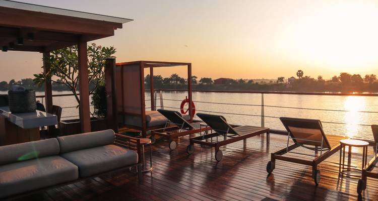 Luxury boat deck with lounge chairs facing a sunset over water.