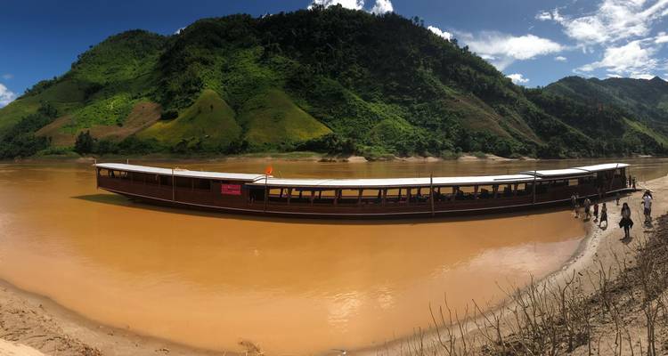 Long boat at a riverbank with people around it.