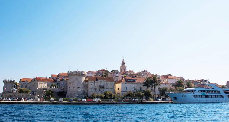 La ligne d'horizon médiévale de Korčula et ses palmiers vus depuis l'eau avec un yacht qui navigue à proximité.