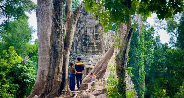 Two people standing before a temple with carved face in tree roots.