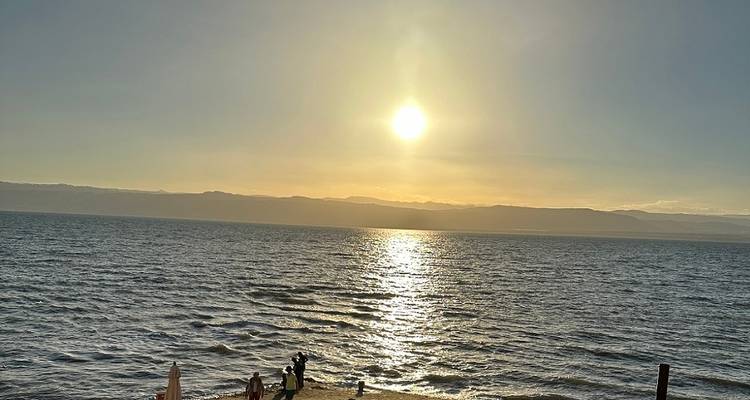 Sunset over a body of water with people on the shore.