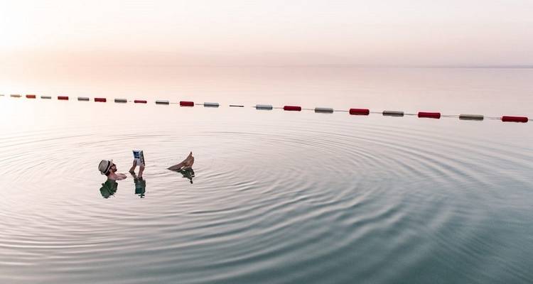 Person floating in the water with reflection during sunset.