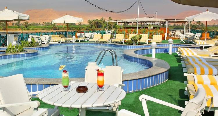 Pool area with lounge chairs and drinks, overlooking a river with distant desert hills.