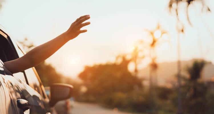 Hand die uit een autoraam steekt met uitzicht op de zonsondergang.