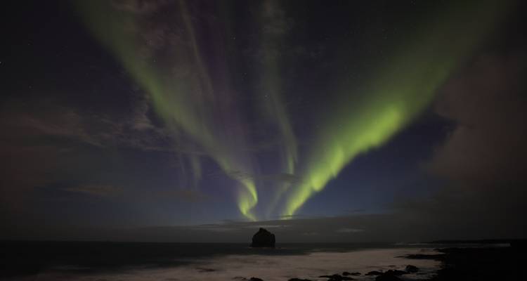 Nordlichter am Himmel über einem Küstengebiet.