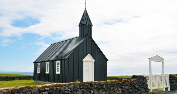 Schwarze Kirche mit umgebender Steinmauer und Grasfeld.