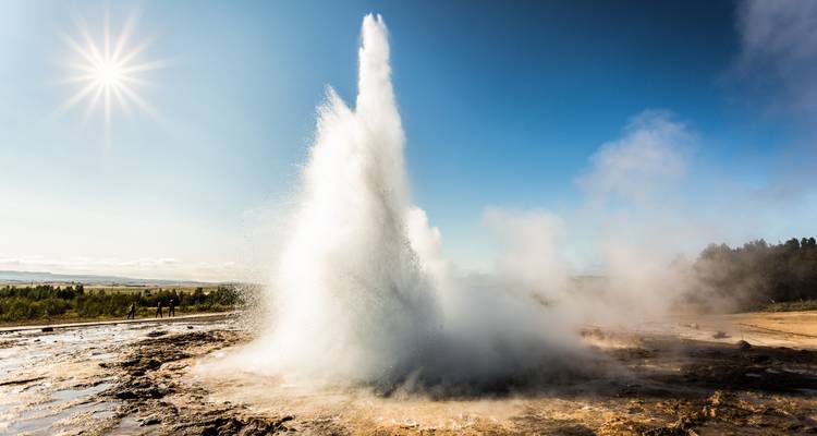 Geysir-Eruption vor klarem blauen Himmel, Sonne sichtbar in der Ecke.