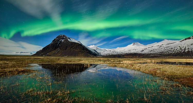Nordlichter über einem Berg mit einer Spiegelung im Wasser.