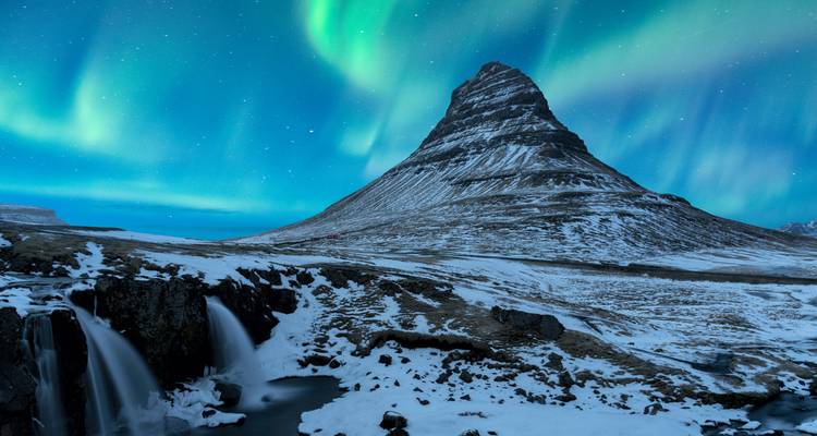 Nordlicht über dem Berg Kirkjufell mit Schnee und einem Wasserfall.