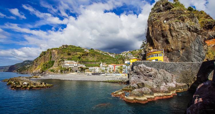 Village côtier avec des maisons colorées et des falaises escarpées au bord de la mer.