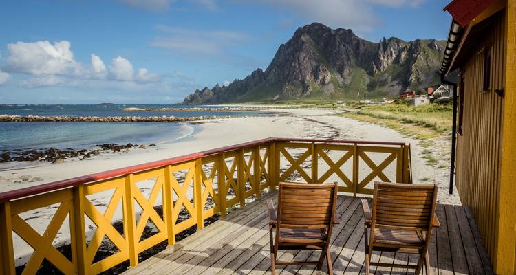Terraza de madera con sillas con vista a una playa con montañas.