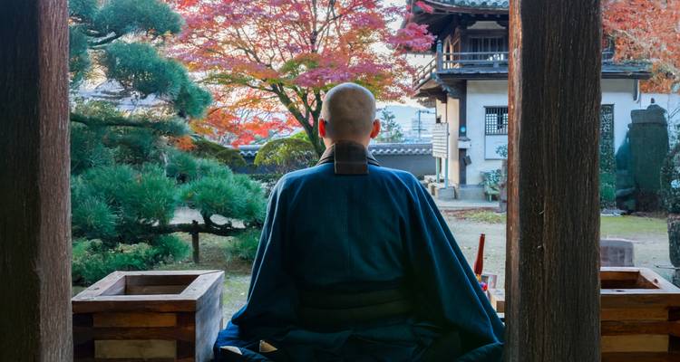 Personne en tenue traditionnelle assise dans un jardin avec une architecture japonaise.