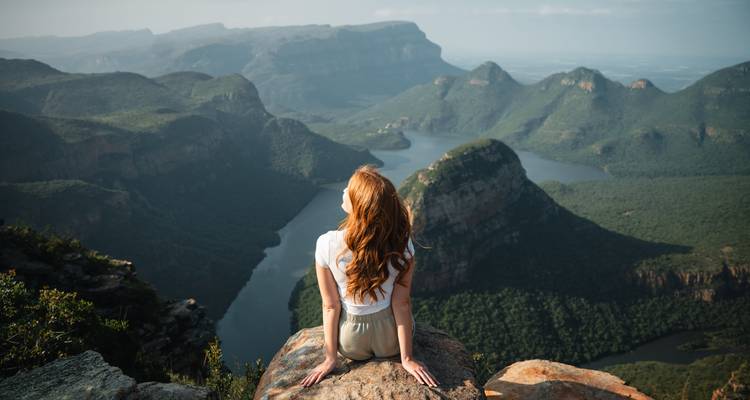 Personne assise sur un rocher contemplant un vaste paysage montagneux.