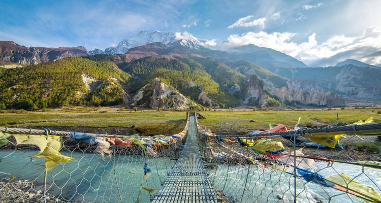 Hängebrücke mit Gebetsfahnen vor einer Bergkulisse.