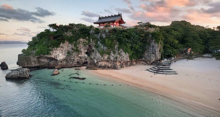 Temple à flanc de falaise surplombant une plage immaculée au coucher du soleil.