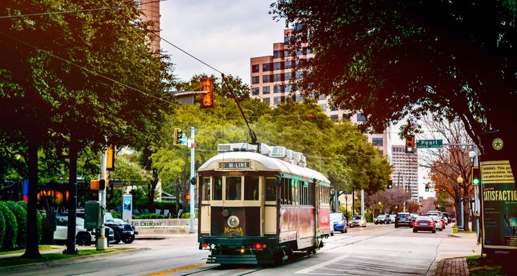 Straat met een historische tram en auto's, omgeven door bomen en gebouwen.
