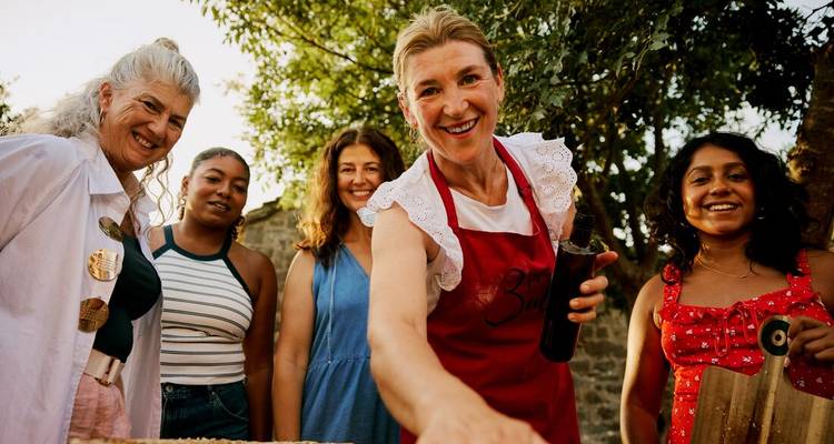 Grupo de mujeres posando al aire libre con una mujer local mostrando botellas.