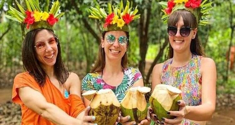 Trois femmes avec des couronnes de fleurs tenant des noix de coco et souriant.