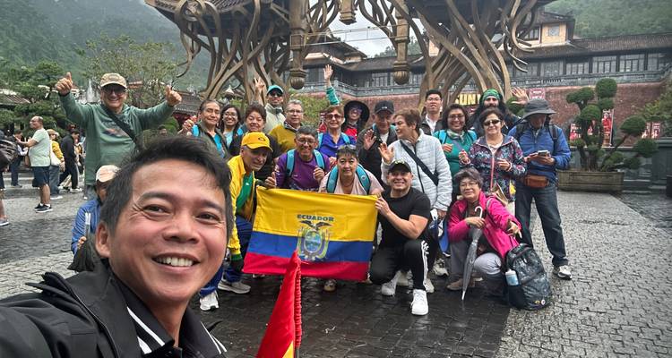 Grupo de viaje animado ondeando una bandera de Ecuador frente a la puerta de madera ornamentada en Sun World Ba Na Hills.
