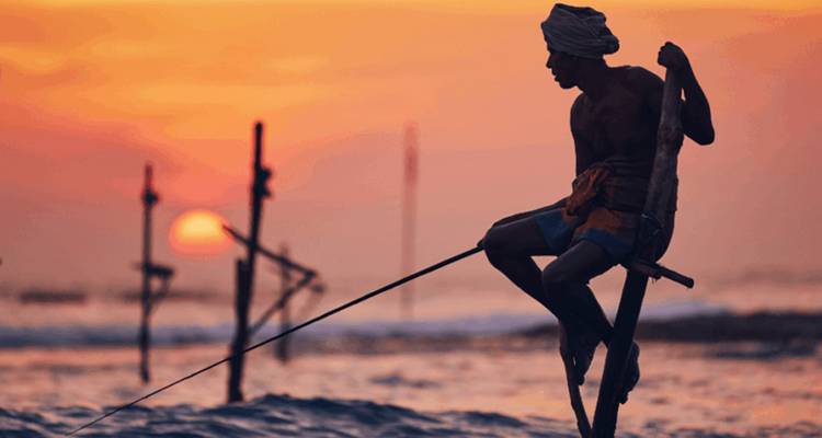 Traditional stilt fisherman fishing at sunset in the ocean.