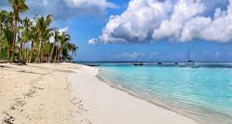 Strand mit weißem Sand und türkisfarbenem Wasser unter einem teilweise bewölkten Himmel.