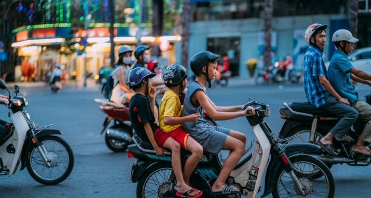 Straatscène met gezinnen die op motoren en scooters door een stedelijk kruispunt rijden tijdens het invallen van de avond.