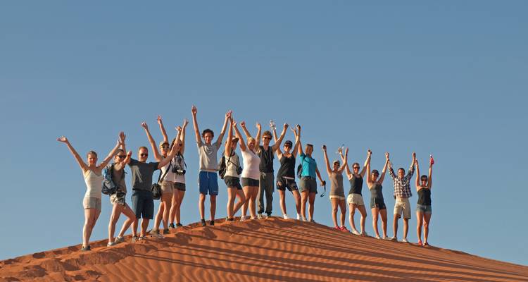 Groupe de personnes debout sur une dune de sable avec les bras levés.