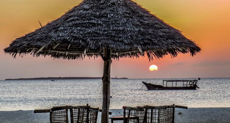 Sunset over the ocean with a traditional boat and thatched umbrella.