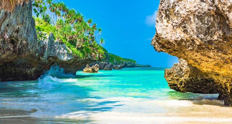 Clear turquoise waters with rocky shoreline and waves.