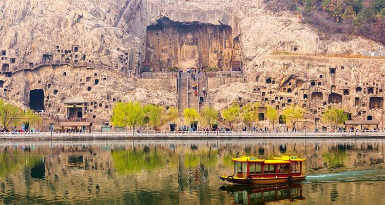 Longmen Grottoes’ cliffside Buddhist carvings reflected in the river with a yellow boat.