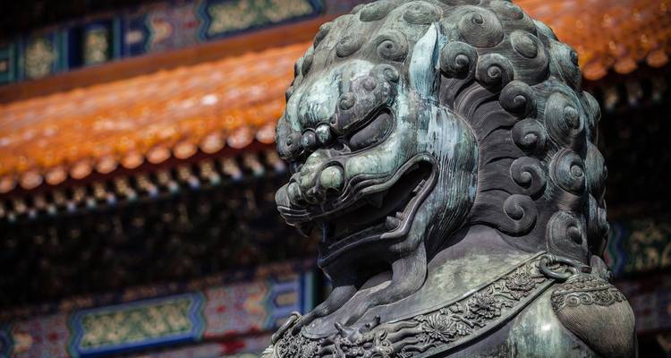 Close detail of bronze guardian lion with ornate background tiles.