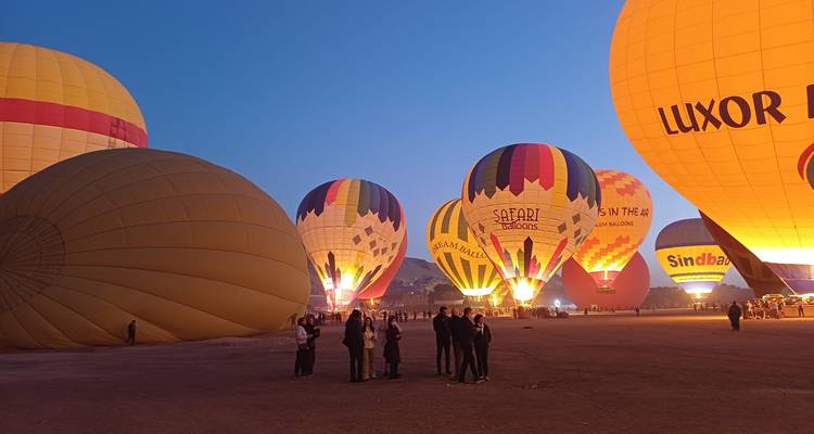 Un campo lleno de globos aerostáticos coloridos iluminándose al atardecer, con grupos de personas reunidas alrededor.