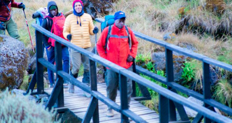 Three hikers crossing a wooden bridge in outdoor gear.