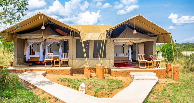 Safaritent met twee kamers en houten stoelen buiten onder een blauwe hemel.