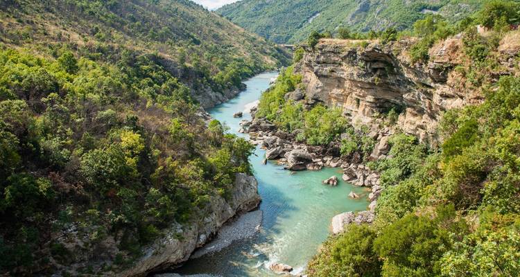 Turquoise rivier slingert door steile groene canyon met rotsachtige kliffen en bossen.