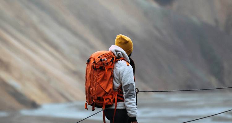 Hiker with an orange backpack standing on a trail.