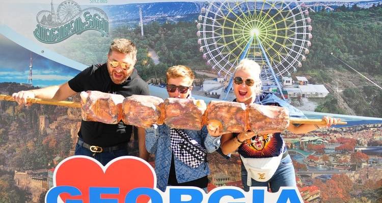 Trois personnes savourant de la viande grillée en grande quantité avec un panneau de la Géorgie.
