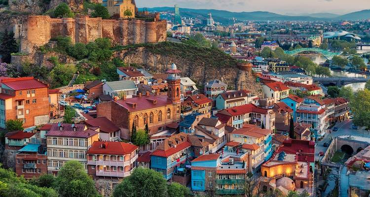 Des bâtiments colorés et des fortifications anciennes dans un paysage vallonné.