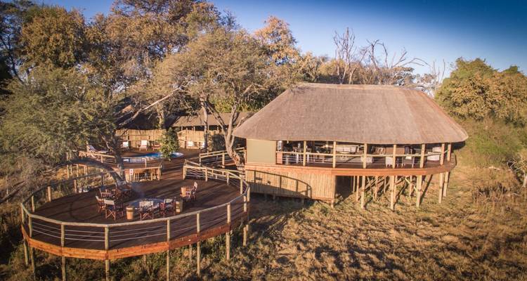 Vue aérienne d'un lodge de safari avec des terrasses en bois surélevées parmi les arbres et les prairies.